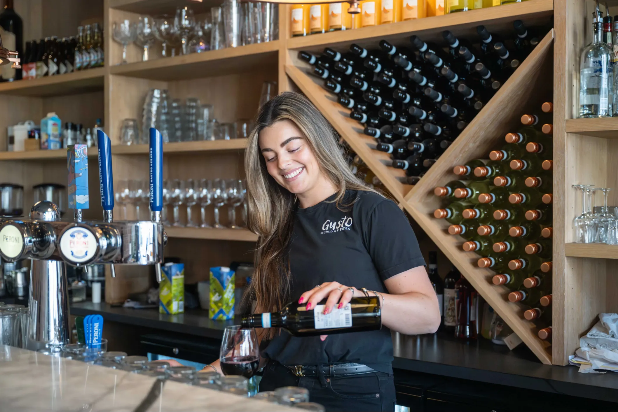 Corporate photo of a woman pouring wine into a glass behind a bar