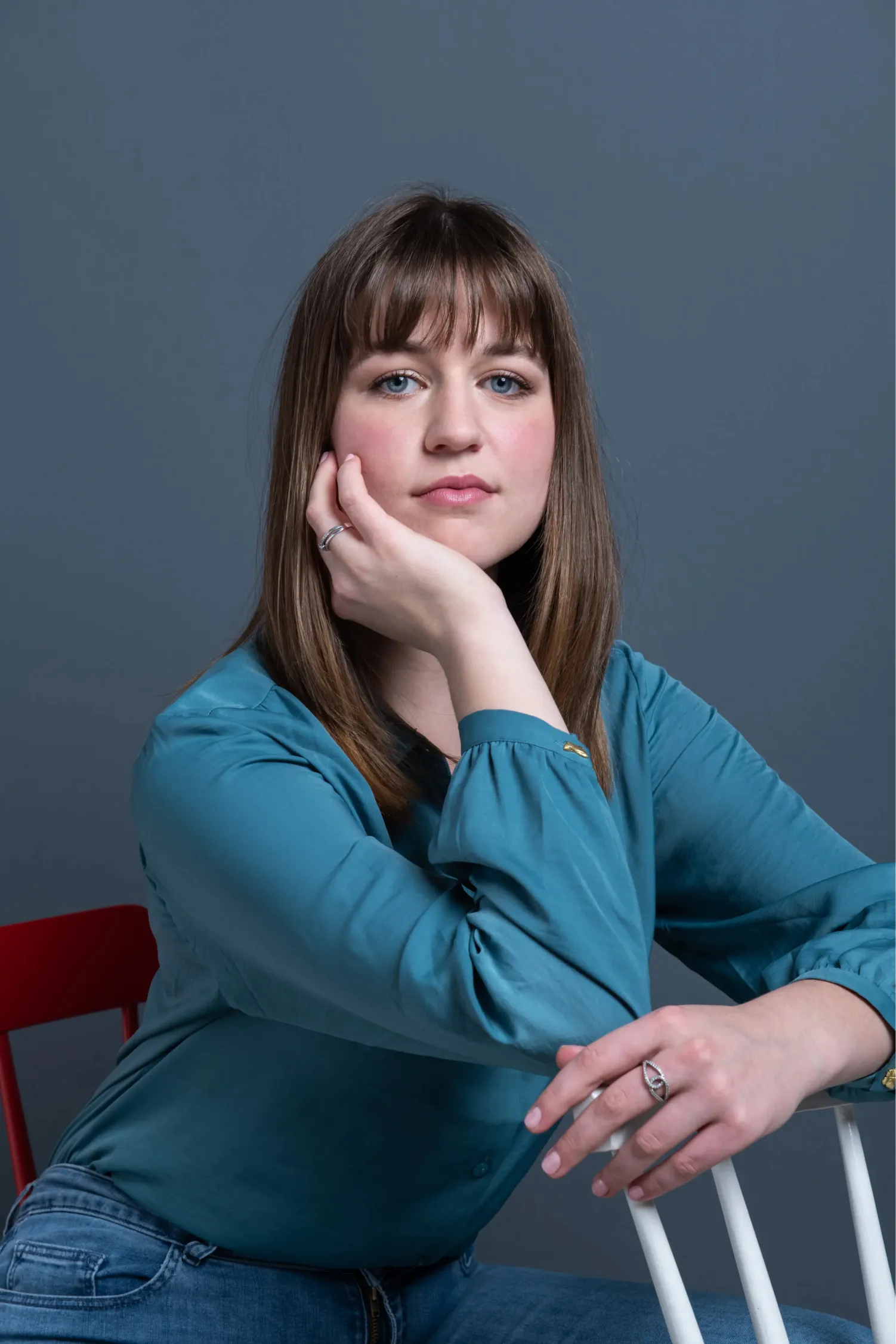 Corporate photo of a woman dressed in blue, seated on a red chair