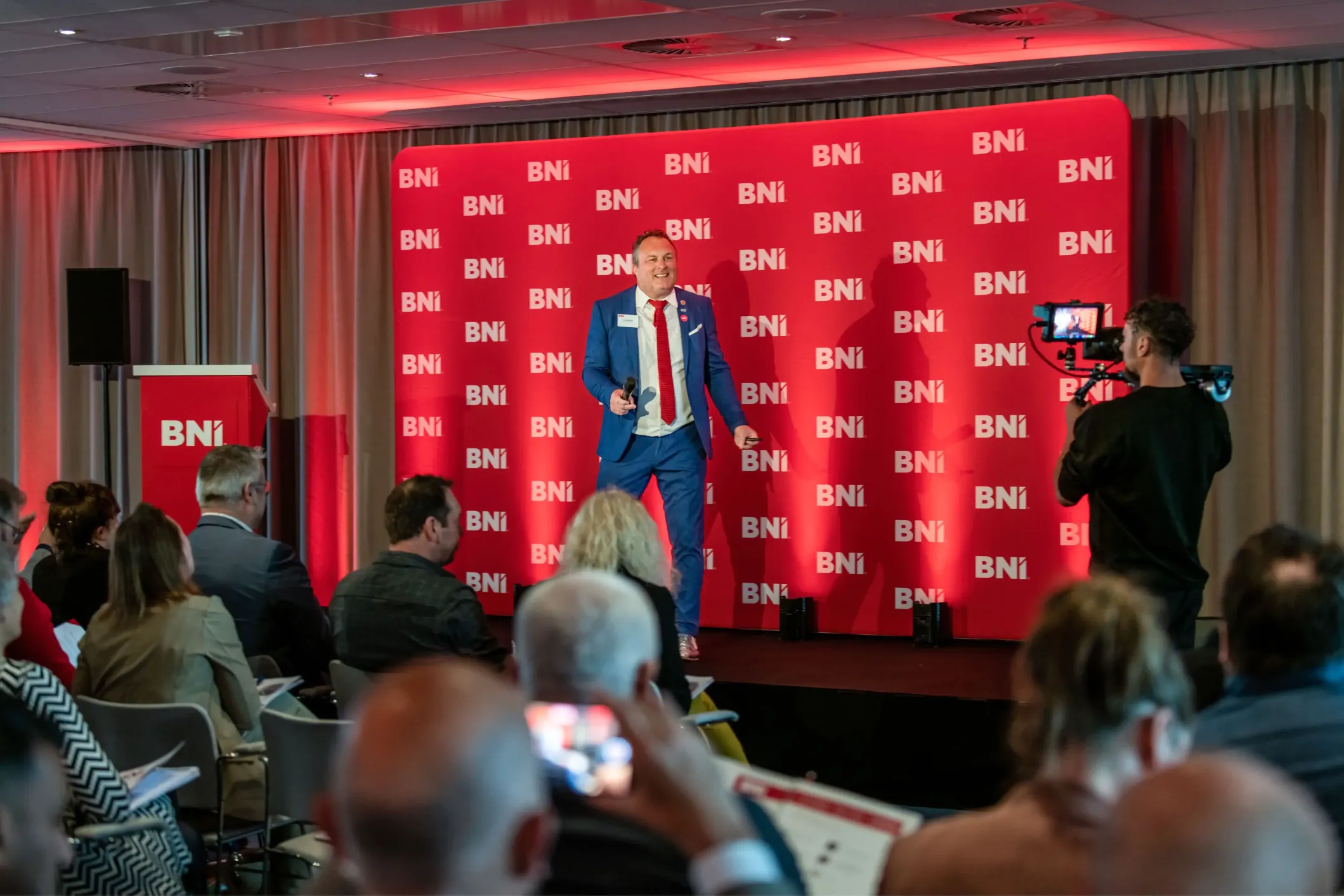 Event photo of a BNI speaker in a blue suit and red tie
