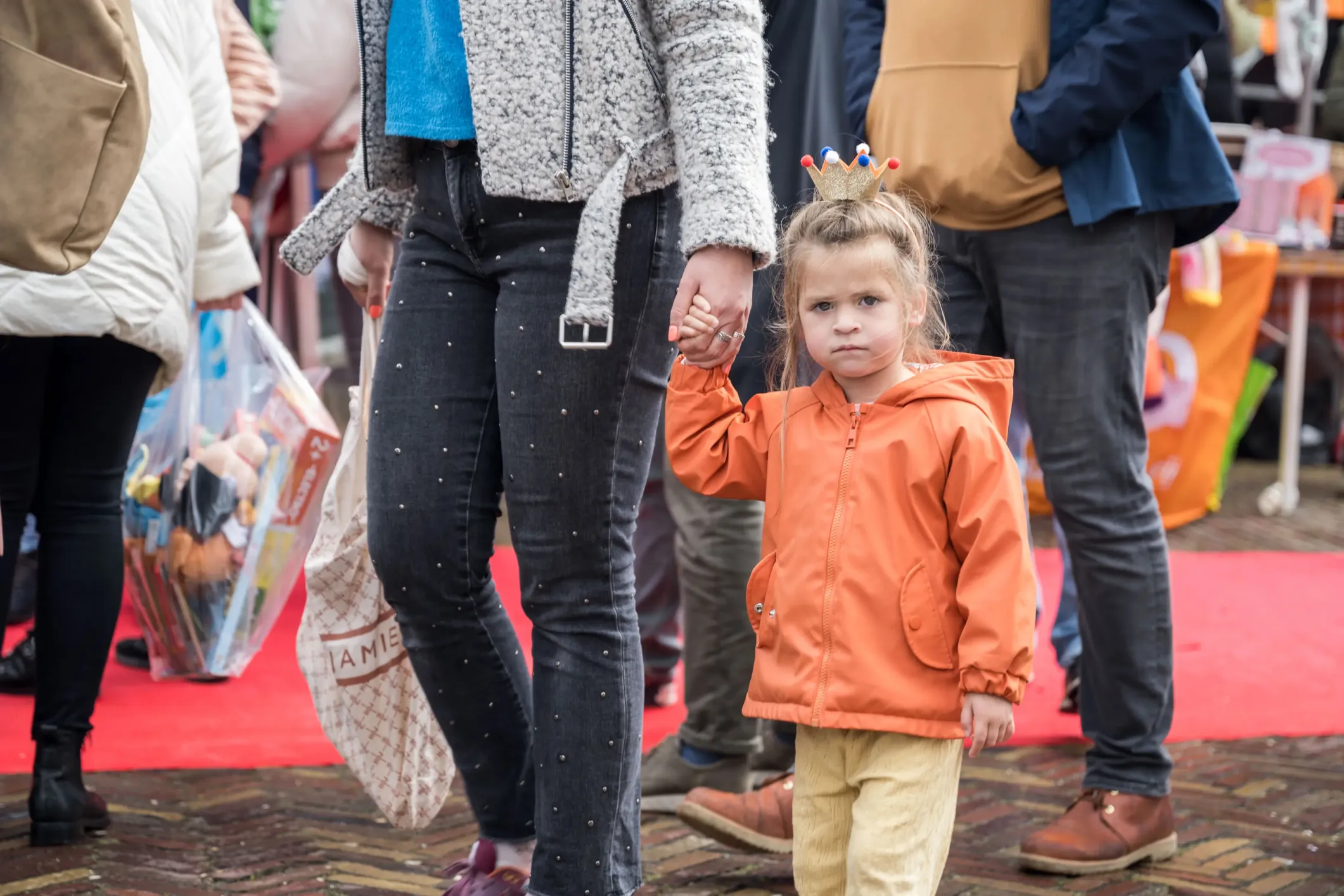 Event photo of a girl in orange on King's Day holding a woman's hand