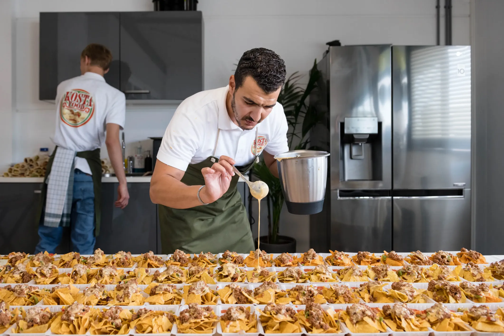 Event photo of a man preparing lots of nacho dishes with cheese sauce