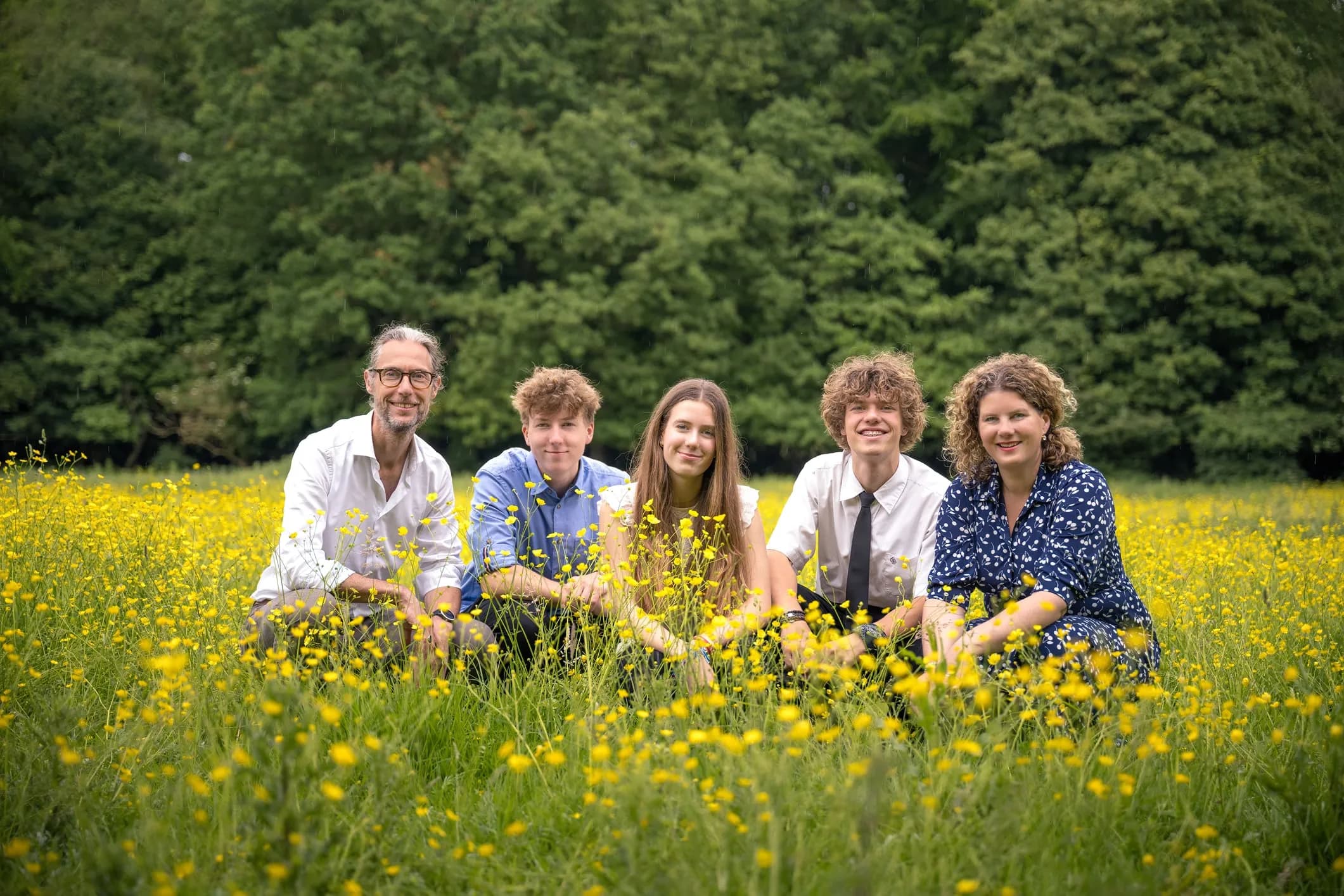 Family photo of parents and three teenagers among yellow flowers on a lawn