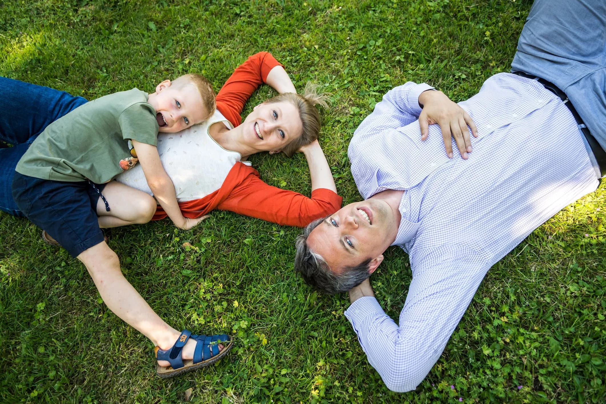 Family photographed from above, lying with their heads together in the grass