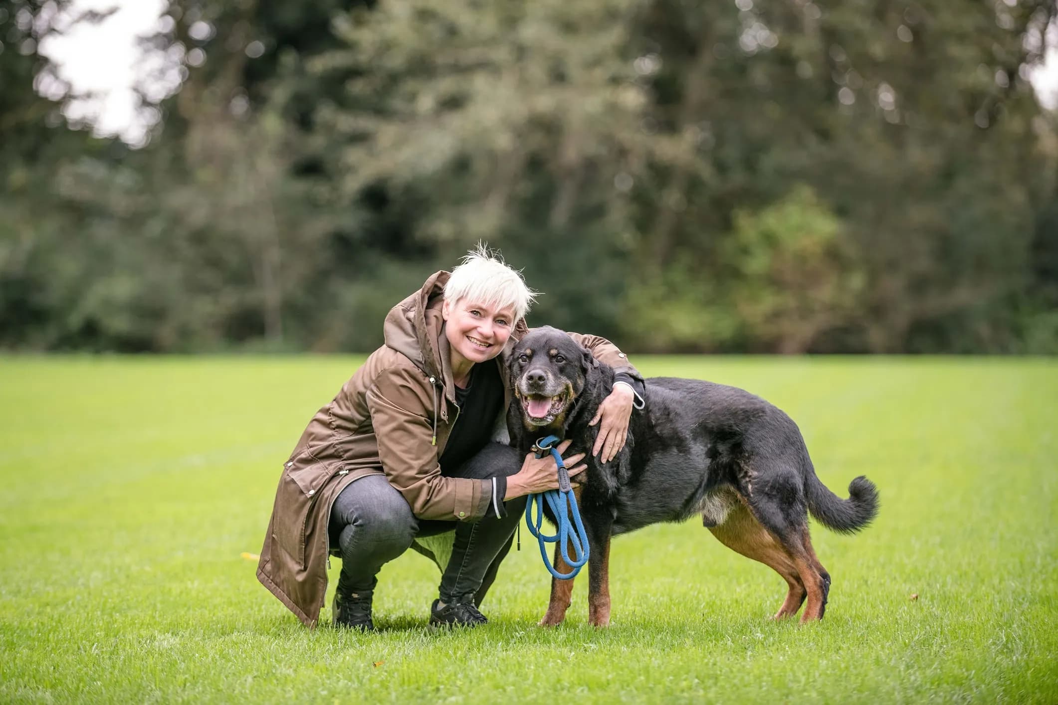 Woman crouching beside her black and brown dog on the grass in the park