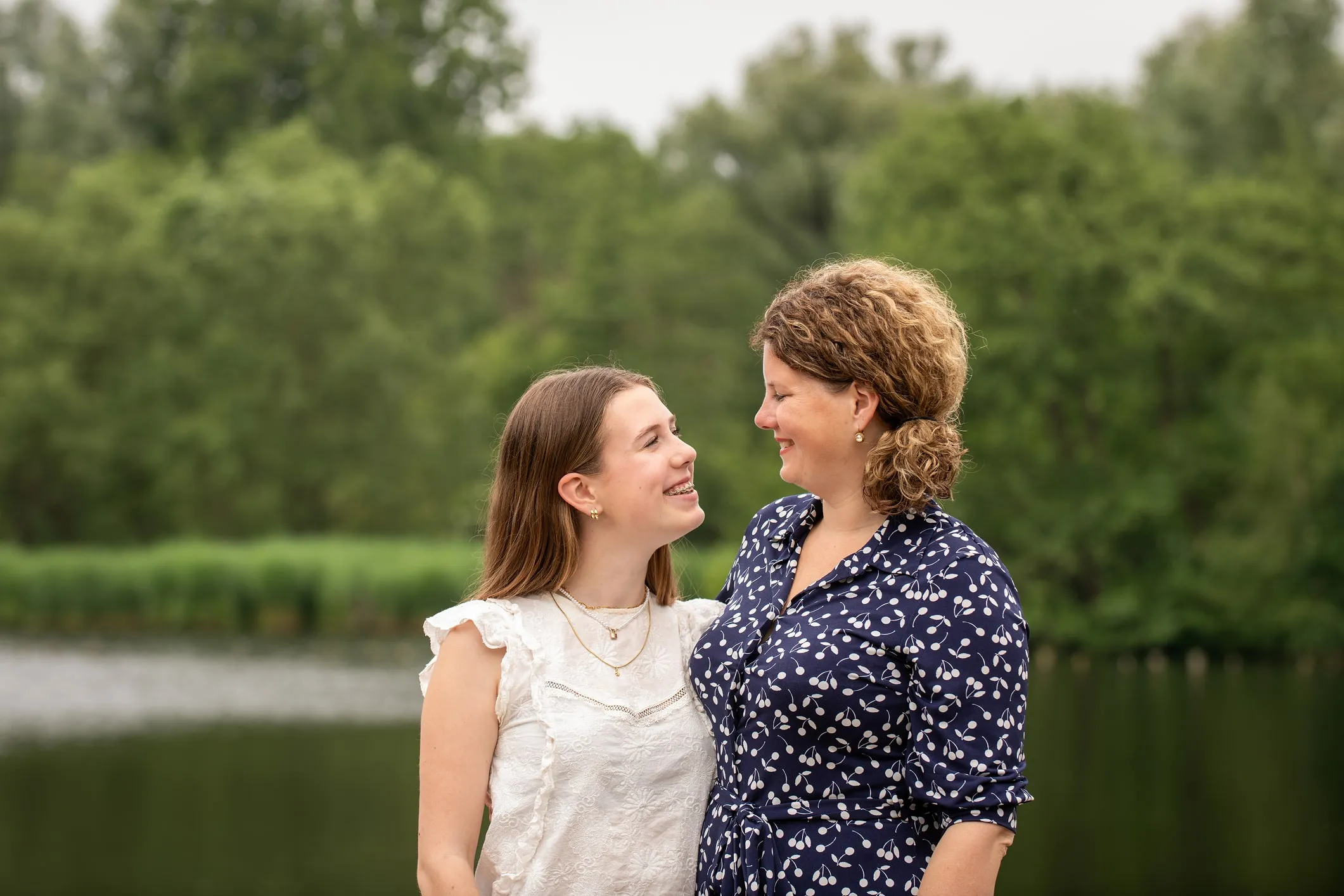 Mother and teenage daughter together at the water's edge, with woods behind them