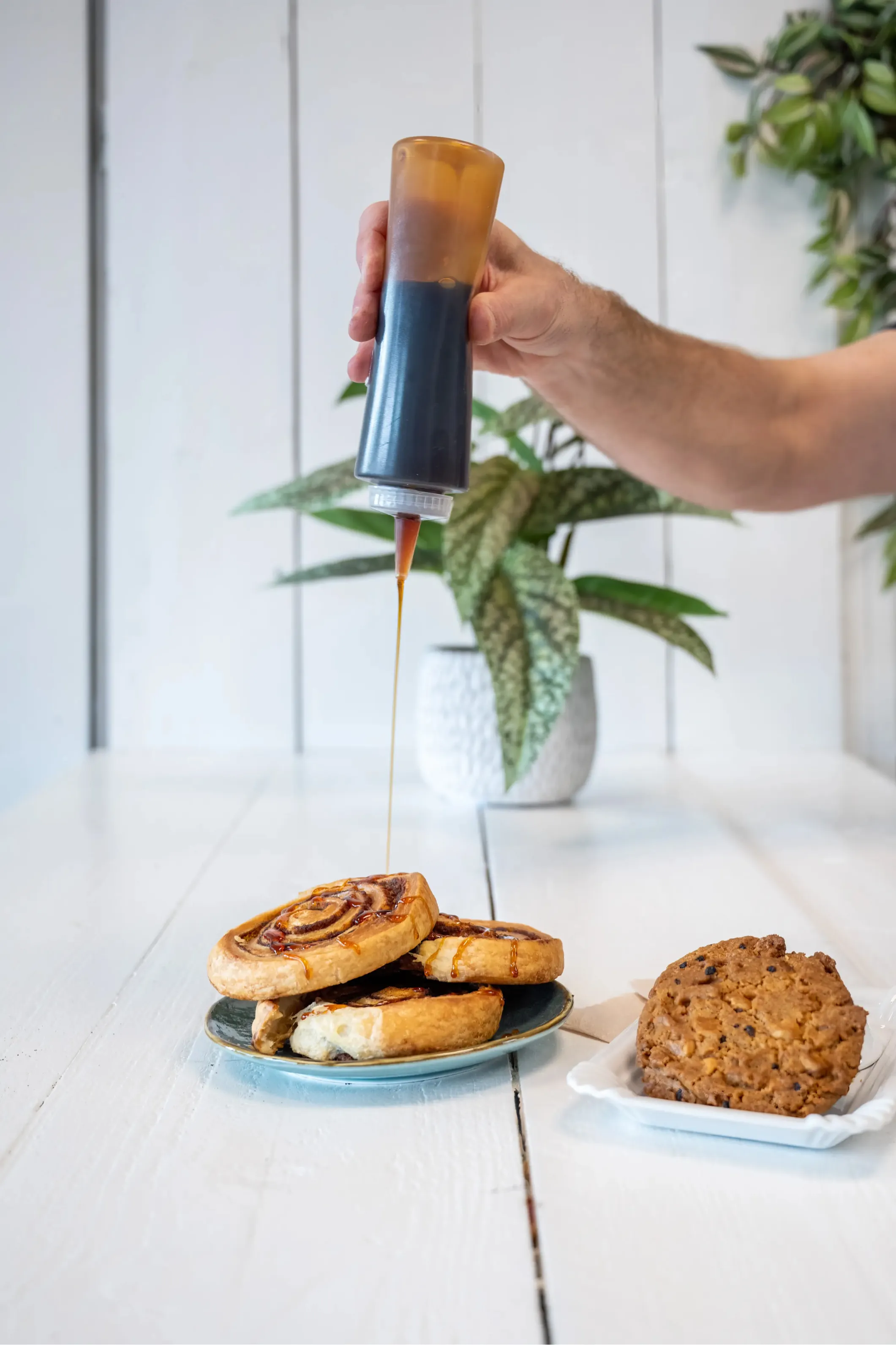 Product photo of a person pouring syrup over cinnamon rolls