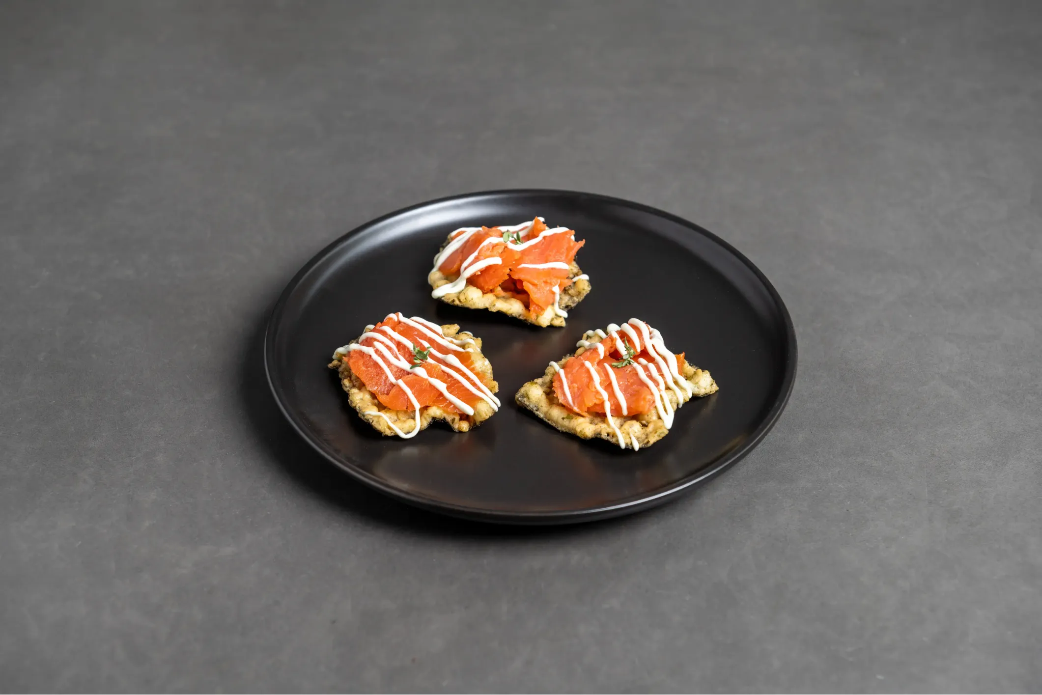 Product photo of crackers with salmon and white sauce on a black plate