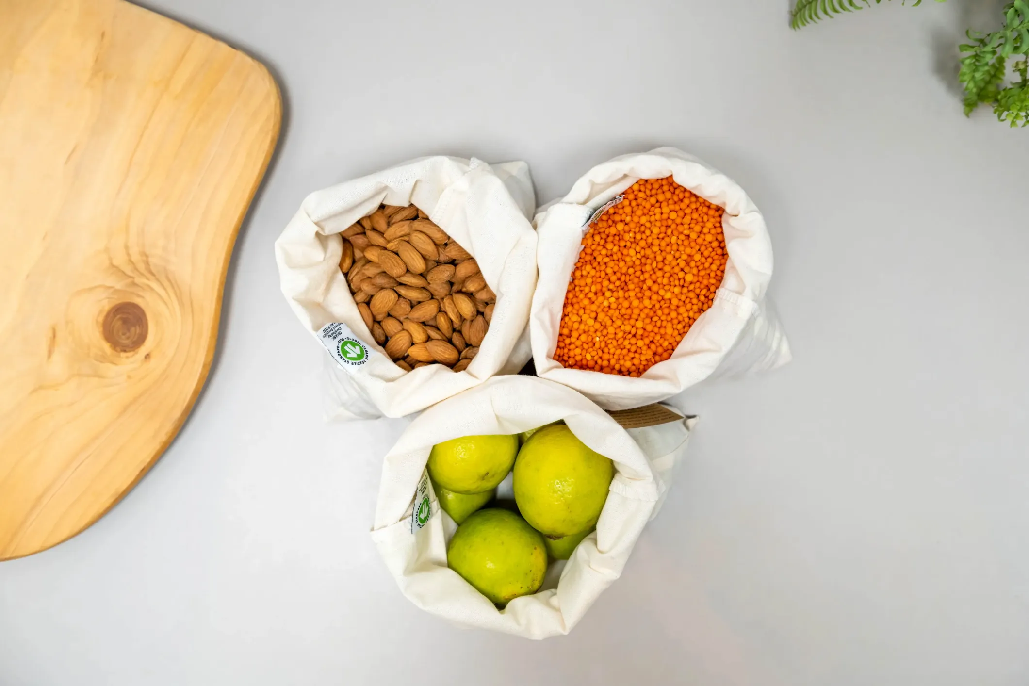 Cotton bags of almonds, red lentils and limes beside a wooden chopping board