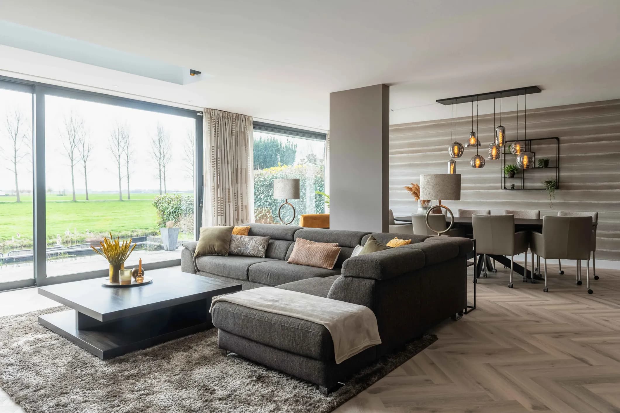 Interior photo of a bright living room with a grey corner sofa and large windows